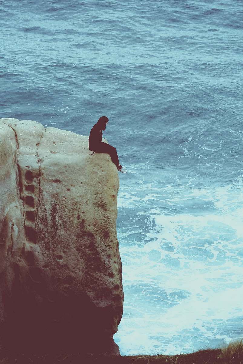 danger person sitting on edge of rock looking at sea water